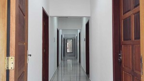 A hallway with wooden doors and a tiled floor, leading to a bright exit. - Pousada Renoah (Ubatuba)