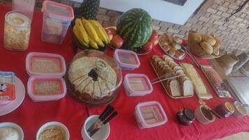 Une table garnie de divers aliments et condiments, notamment des fruits, du pain et des pots de confitures.