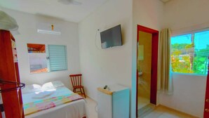 A bedroom with a bed, a desk, a chair, a TV, and a window with a view of greenery. - Pousada Renoah (Ubatuba)