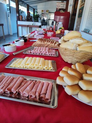 A buffet table with various food items including rolls, bread, and sliced meats.
