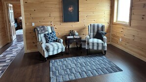 Une pièce chaleureuse aux murs et au plancher en bois, comprenant deux fauteuils à rayures, une petite table avec une lampe et un tapis.