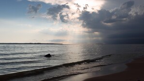 Une plage avec des vagues, une terre lointaine à l’horizon et un ciel nuageux.