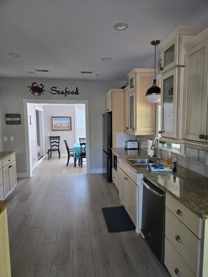 Una cocina con armarios de madera, un refrigerador, un lavavajillas y un comedor con mesa y sillas.