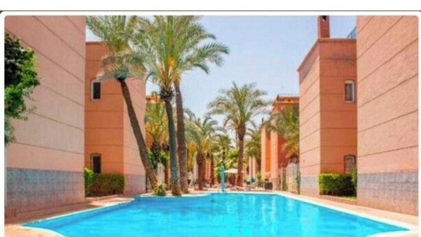 A swimming pool surrounded by palm trees and buildings with a tiled floor. - Family Riad in Marrakech for 6 people (Marrakech)