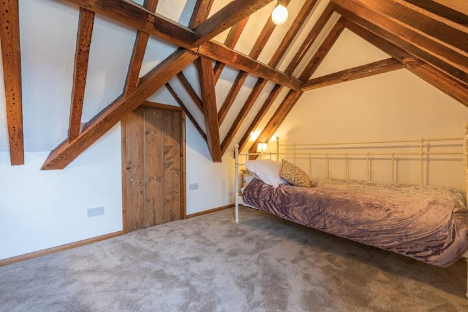 Een slaapkamer met een schuine hemel, zichtbare houten balken, een enkel bed en een deur.