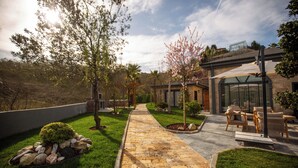 Un chemin pavé mène à un bâtiment à la façade en verre, entouré de verdure et doté d’un espace de repos extérieur.