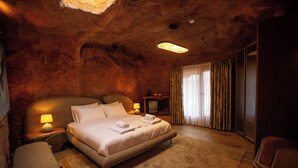 Une chambre avec un grand lit, une table de chevet avec une lampe, un plancher en bois et un mur en pierre.