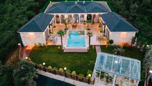 Une grande maison à deux étages avec une piscine, entourée d’une pelouse bien entretenue et d’une serre.