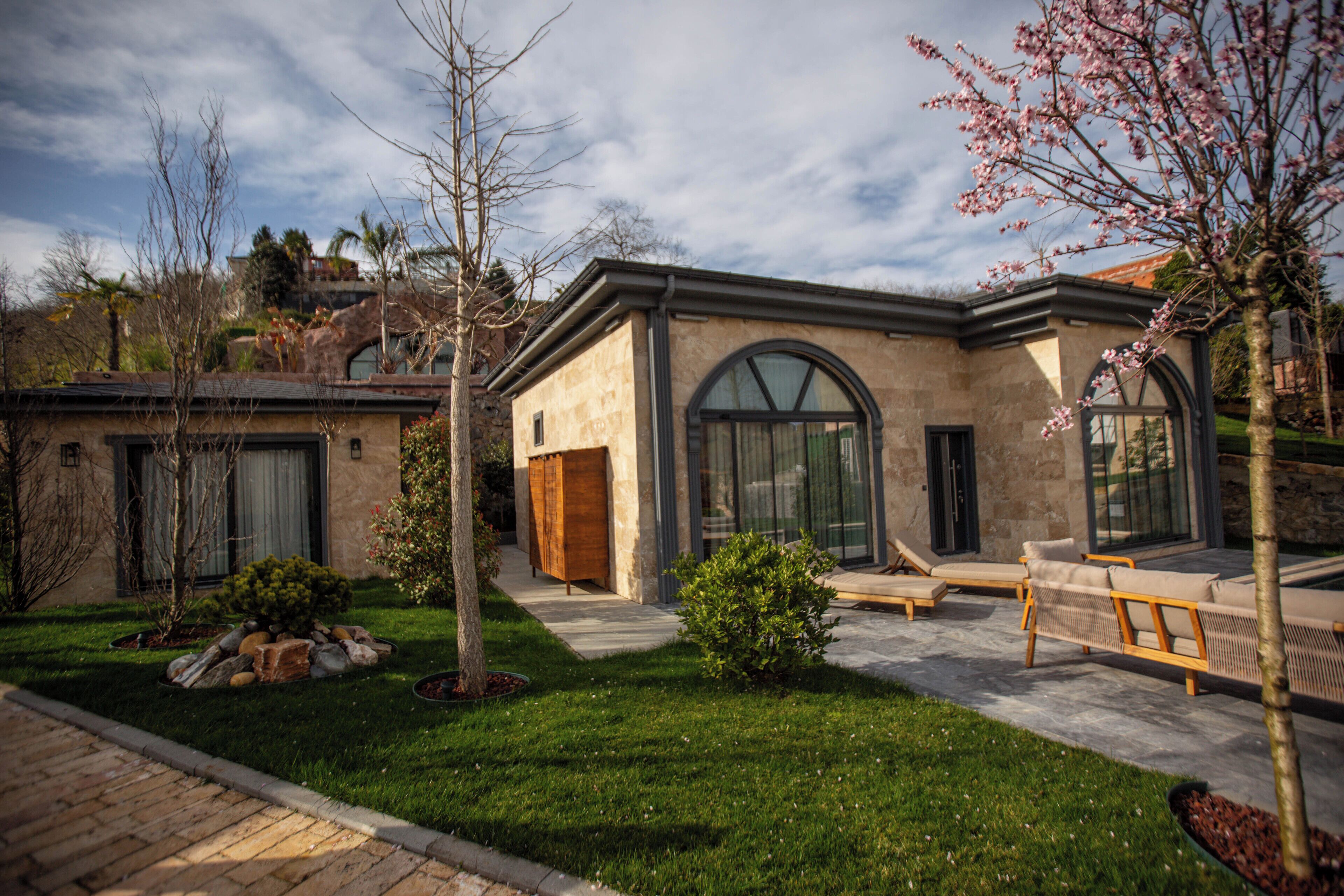 A modern house with a stone facade, large arched windows, and a well-maintained lawn.