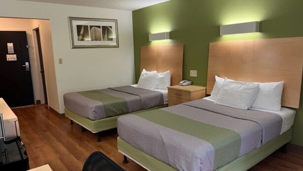 A hotel room with two beds, a desk, a chair, and a door. - Suburban Studios (Coraopolis)