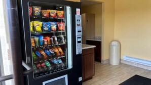 A vending machine with snacks and drinks in a room with wooden cabinets and a trash can. - Suburban Studios (Coraopolis)