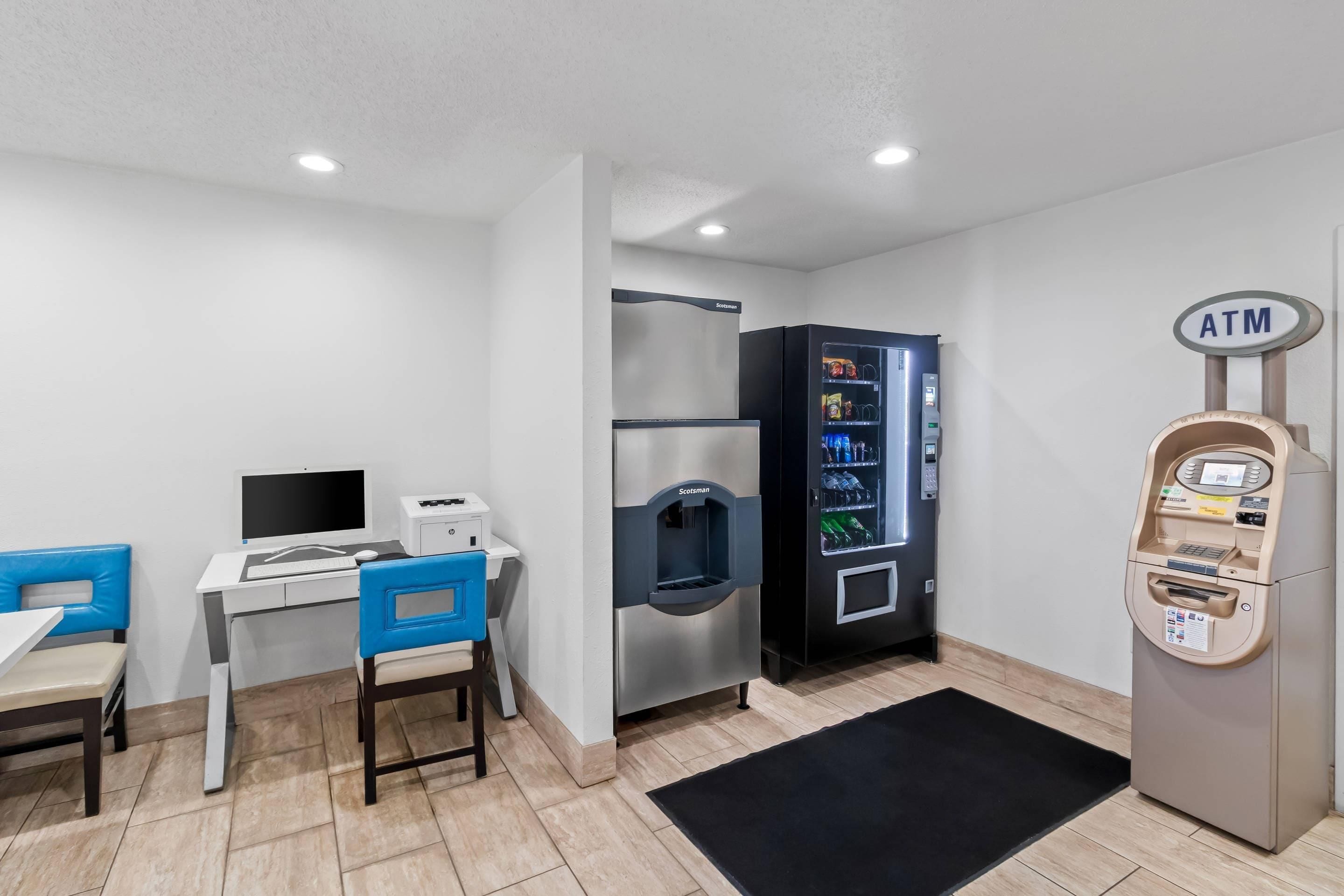 A room with a desk, chairs, a refrigerator, a vending machine, and an ATM.