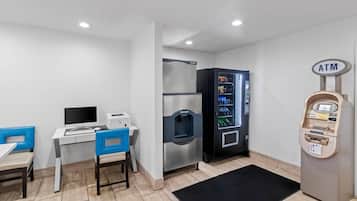 Una habitación con escritorio, sillas, refrigerador, máquina expendedora y cajero automático.