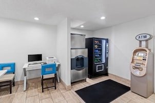 Una habitación con escritorio, sillas, refrigerador, máquina expendedora y cajero automático.