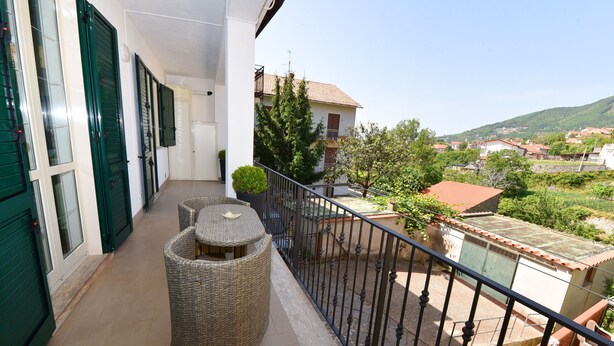 Un balcone con mobili in vimini, vista su una zona residenziale e ringhiera in metallo.