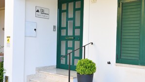 Un ingresso di un edificio con una porta verde, una pianta in vaso e un cartello con il nome della struttura.