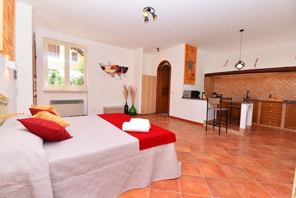 Quarto com uma cama, um cobertor vermelho e um travesseiro vermelho. Há uma janela com vista para o exterior.