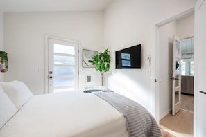 Un dormitorio con cama, televisión montada en la pared, una puerta y una planta.