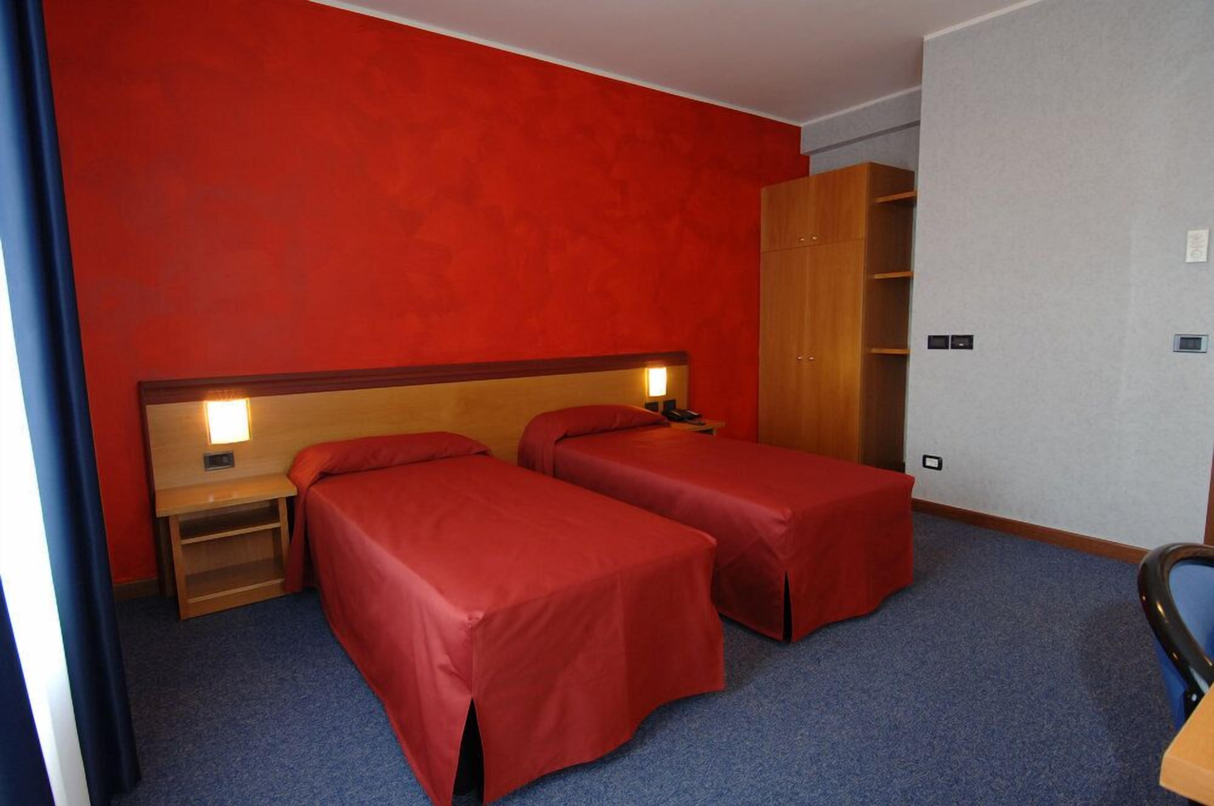 Quarto de hotel com duas camas de solteiro, um guarda-roupa de madeira e uma escrivaninha com cadeira.