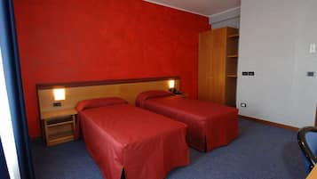 Quarto de hotel com duas camas de solteiro, um guarda-roupa de madeira e uma escrivaninha com cadeira.