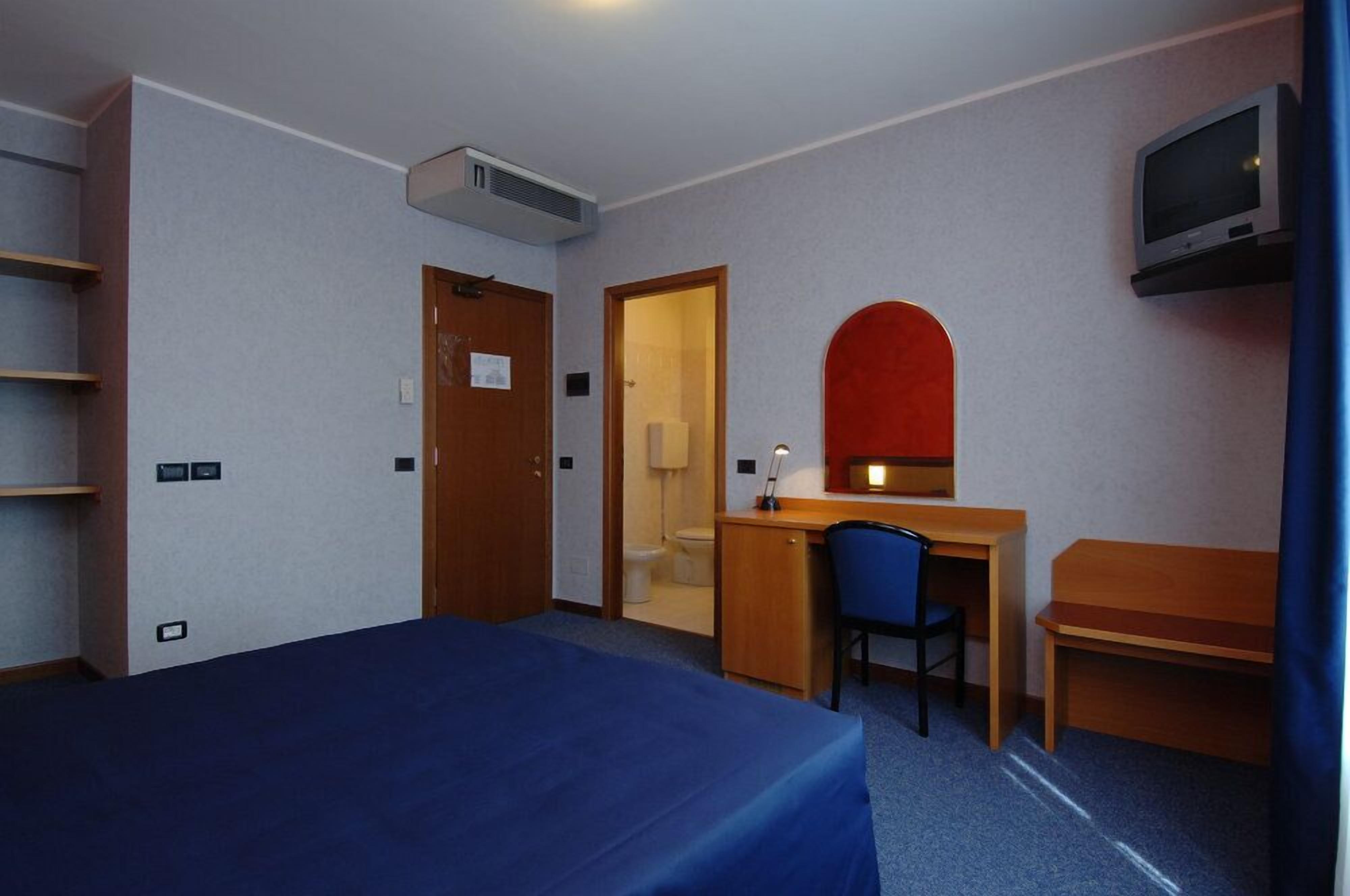 A hotel room with a bed, desk, chair, and a television mounted on the wall.