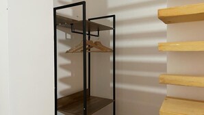 Una habitación con un armario metálico negro, estantes de madera y un perchero de madera.