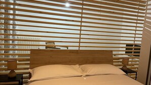 Un dormitorio con cabecera de madera, cama con ropa blanca y mesita de noche con lámpara.