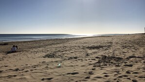Een strand met voetafdrukken en een persoon die op het zand zit.