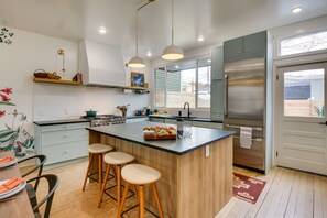 Eine moderne Küche mit Kochinsel, Barhocker, einem Edelstahl-Kühlschrank und einem Fenster, das für natürliches Licht sorgt.