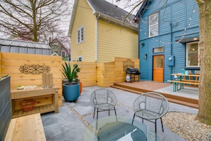 Eine Terrasse mit Holzzaun, einem Glastisch, zwei Korbstühlen, einem Blumentopf und einem Grill.