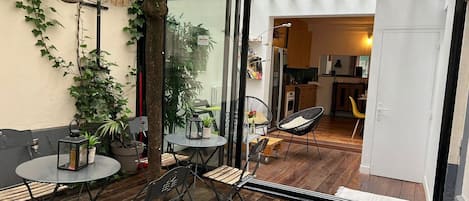 A patio with wooden flooring, metal chairs, a round table, and potted plants.
