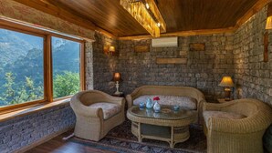 Una habitació acollidora amb mobles de vimet, una paret de pedra i un gran finestral que ofereix vistes a la muntanya.