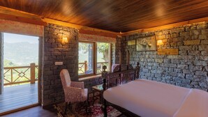 Un dormitori amb paret de pedra, sostre de fusta, un llit gran, escriptori, cadira i vista a l'exterior.