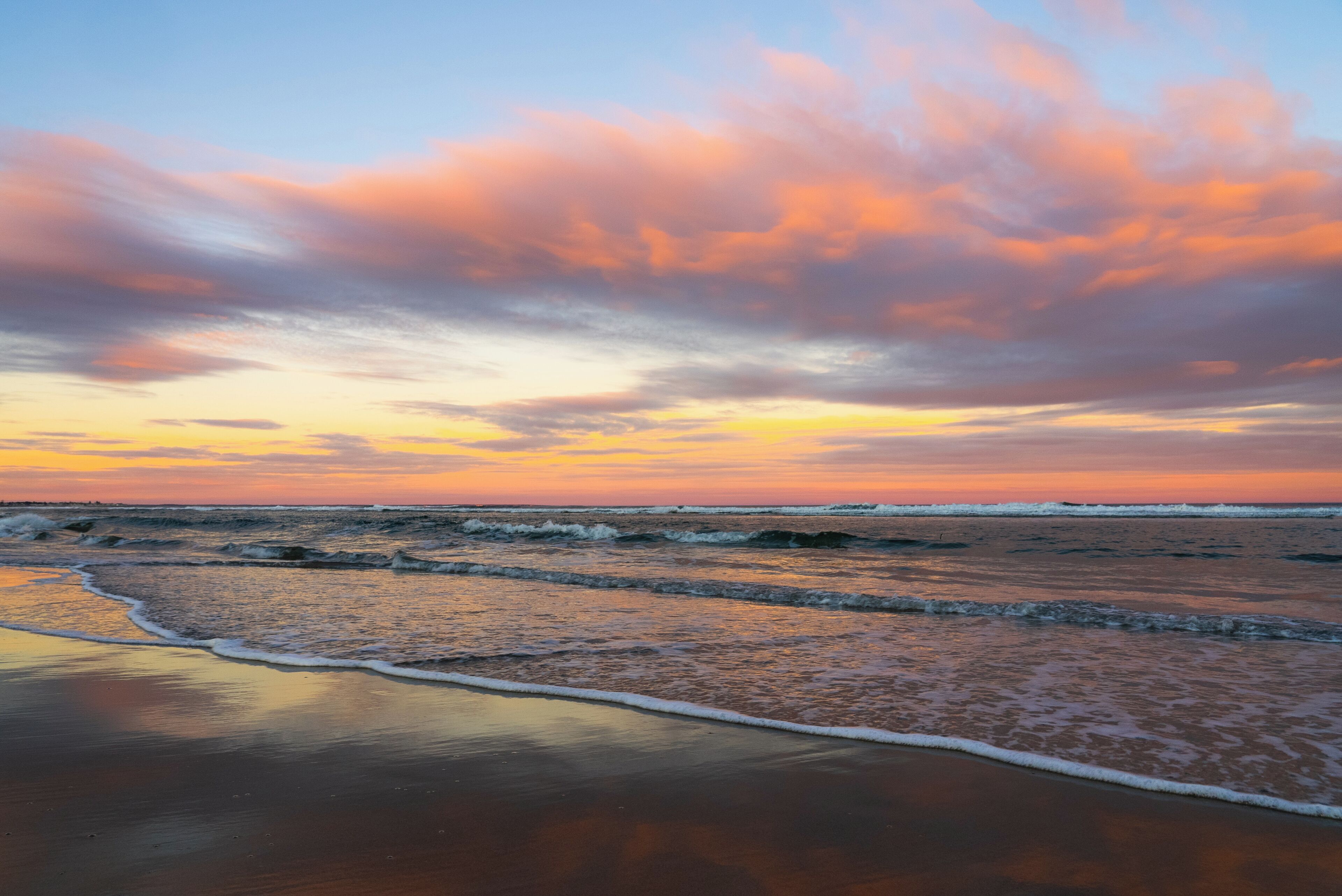 A beach with waves and a sunset sky.