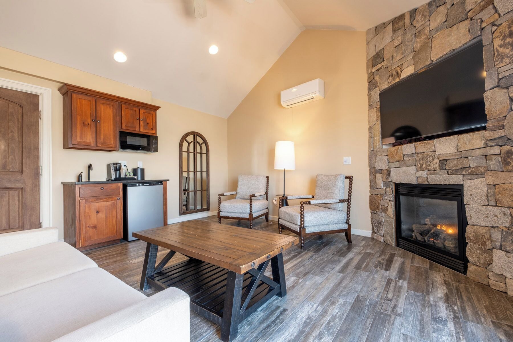 A living room with a stone fireplace, a dining table, and a kitchen area with wooden cabinets and a microwave.
