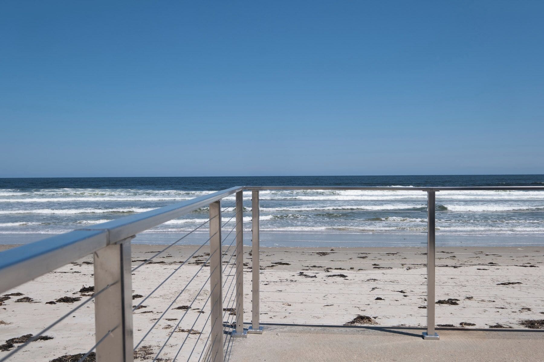 Vista de la playa con barandilla metálica, arena y olas del océano.