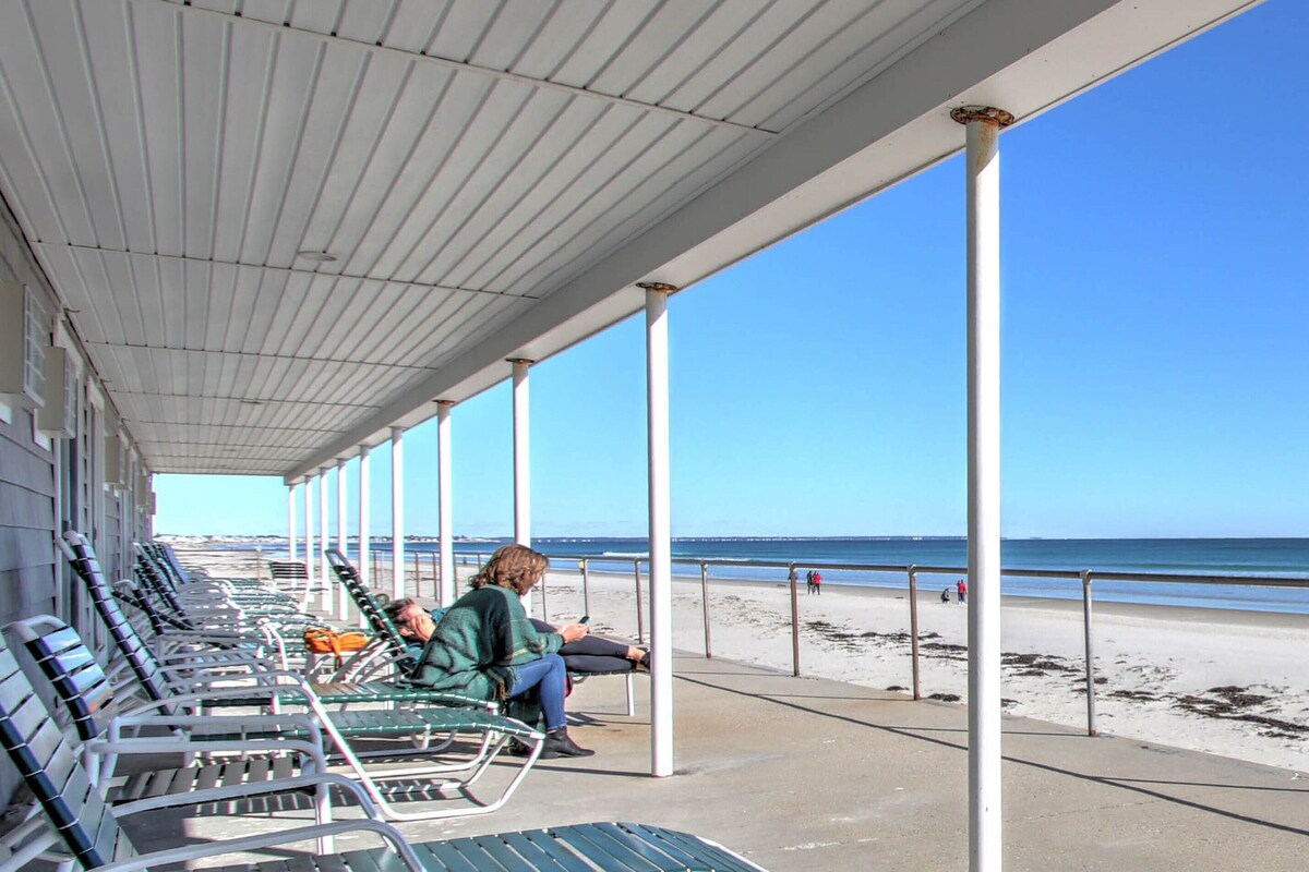 A covered seating area with metal chairs and a person using a mobile device.