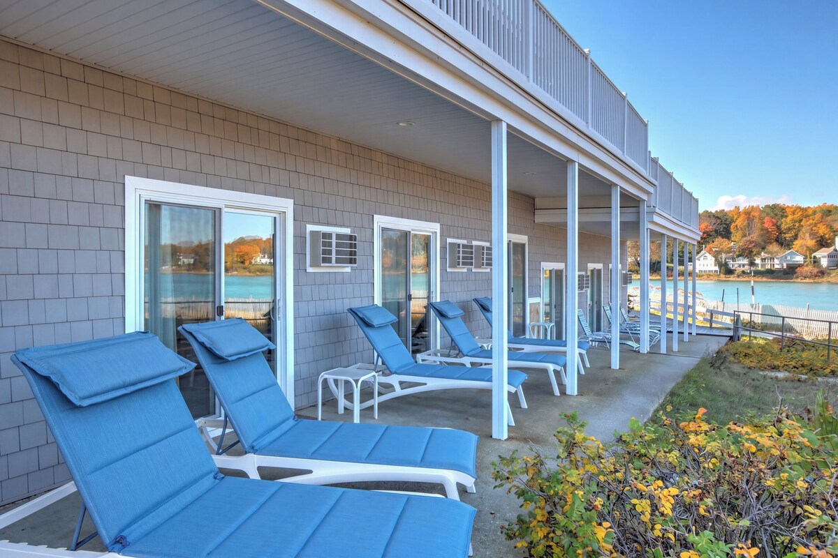 A building with a covered outdoor area featuring lounge chairs and a view of a body of water.