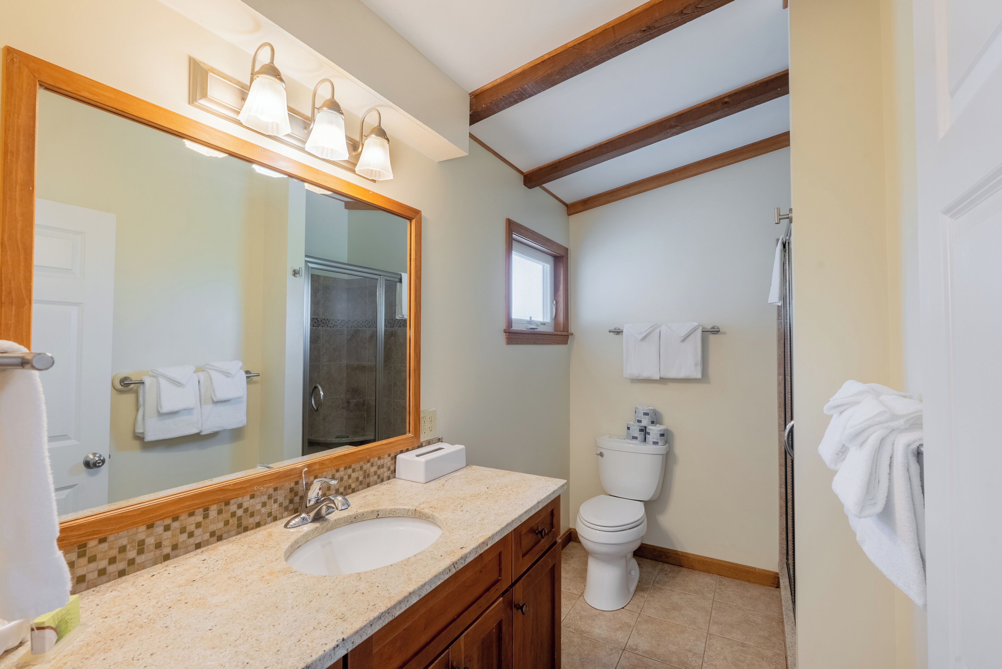 A bathroom with a large mirror, two sinks, a toilet, and a shower.