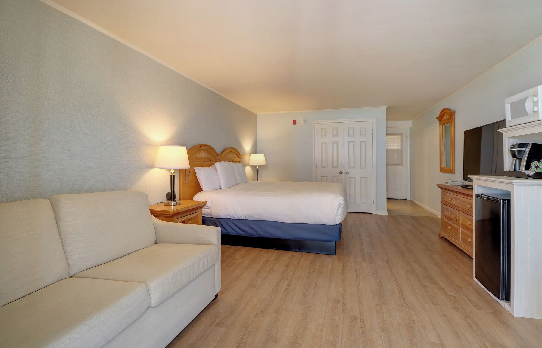 Una habitación de hotel con una cama, un sofá, un escritorio y una cafetera, además de un espejo.