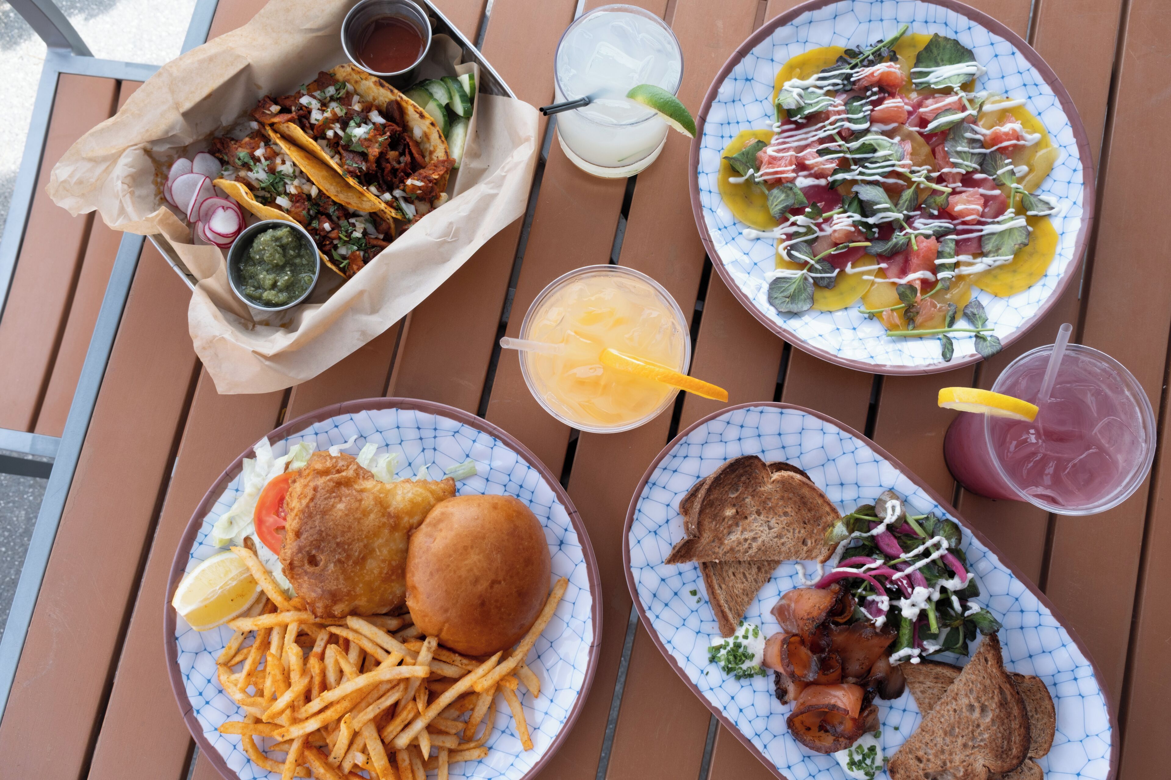 A table with various dishes including a fish sandwich, fries, a salad, and tacos.