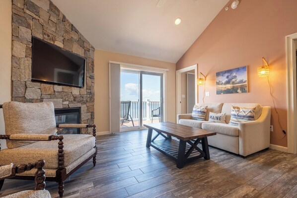 A living room with a stone fireplace, a sofa, a coffee table, and a television mounted on the wall. - Norseman Resort (Ogunquit)