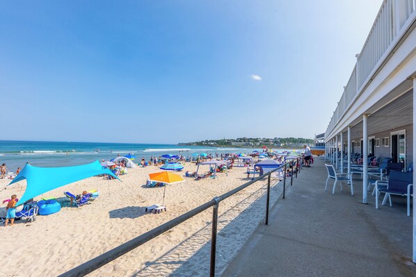 Un hotel frente a la playa con arena, sombrillas, sillas de descanso y vista al océano.