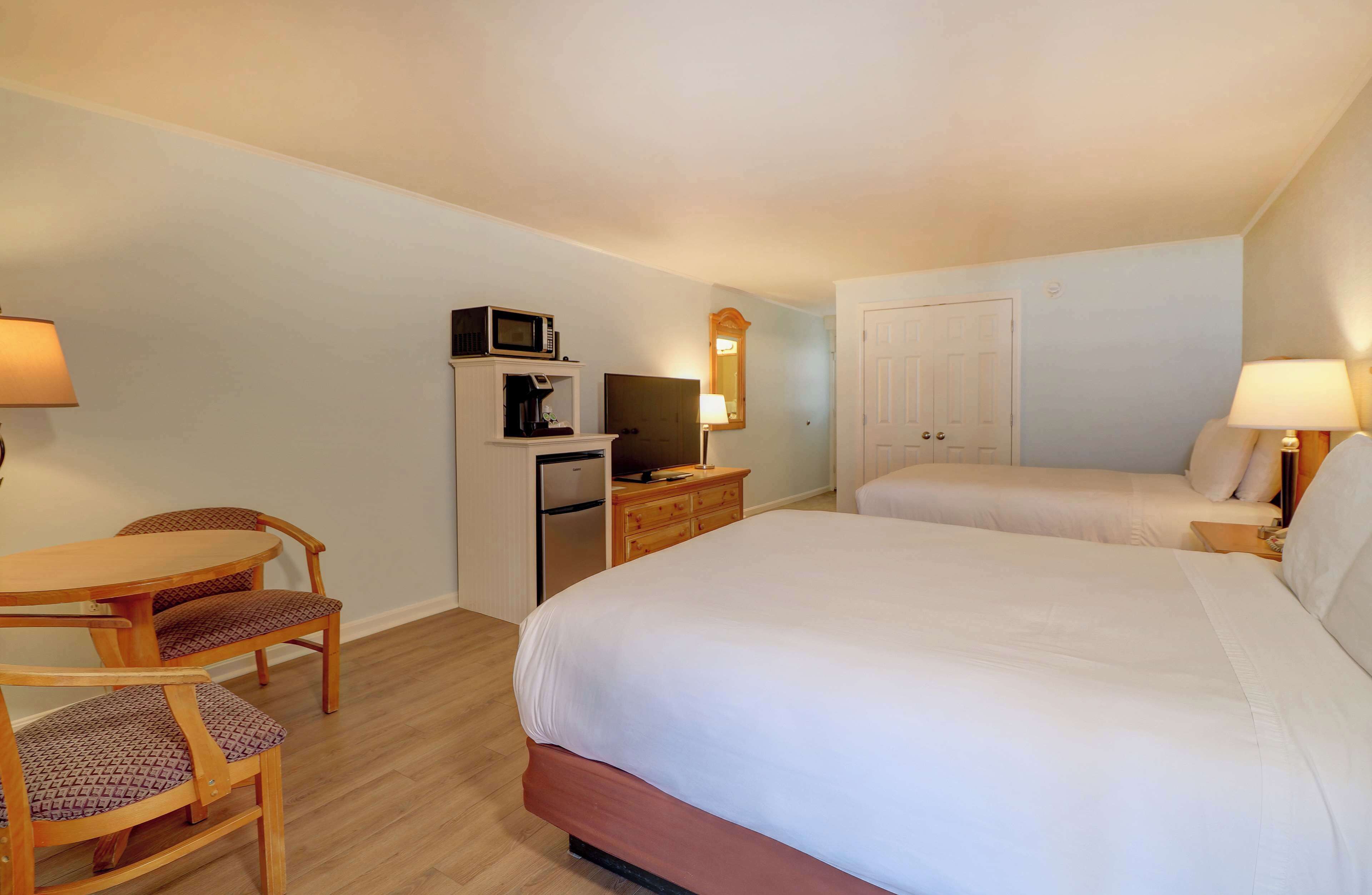 A hotel room with a bed, a desk, a chair, a microwave, a television, and a wardrobe.