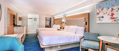 Una habitación de hotel con dos camas, un escritorio, una silla, una mesita y un cuadro en la pared.