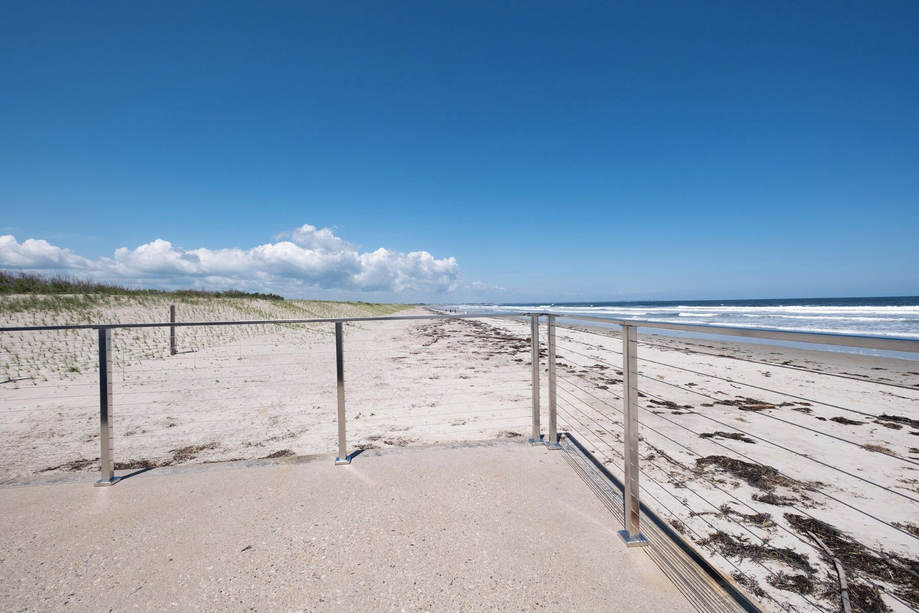 Una playa con un paseo marítimo de concreto y barandillas de metal, que conduce al océano.