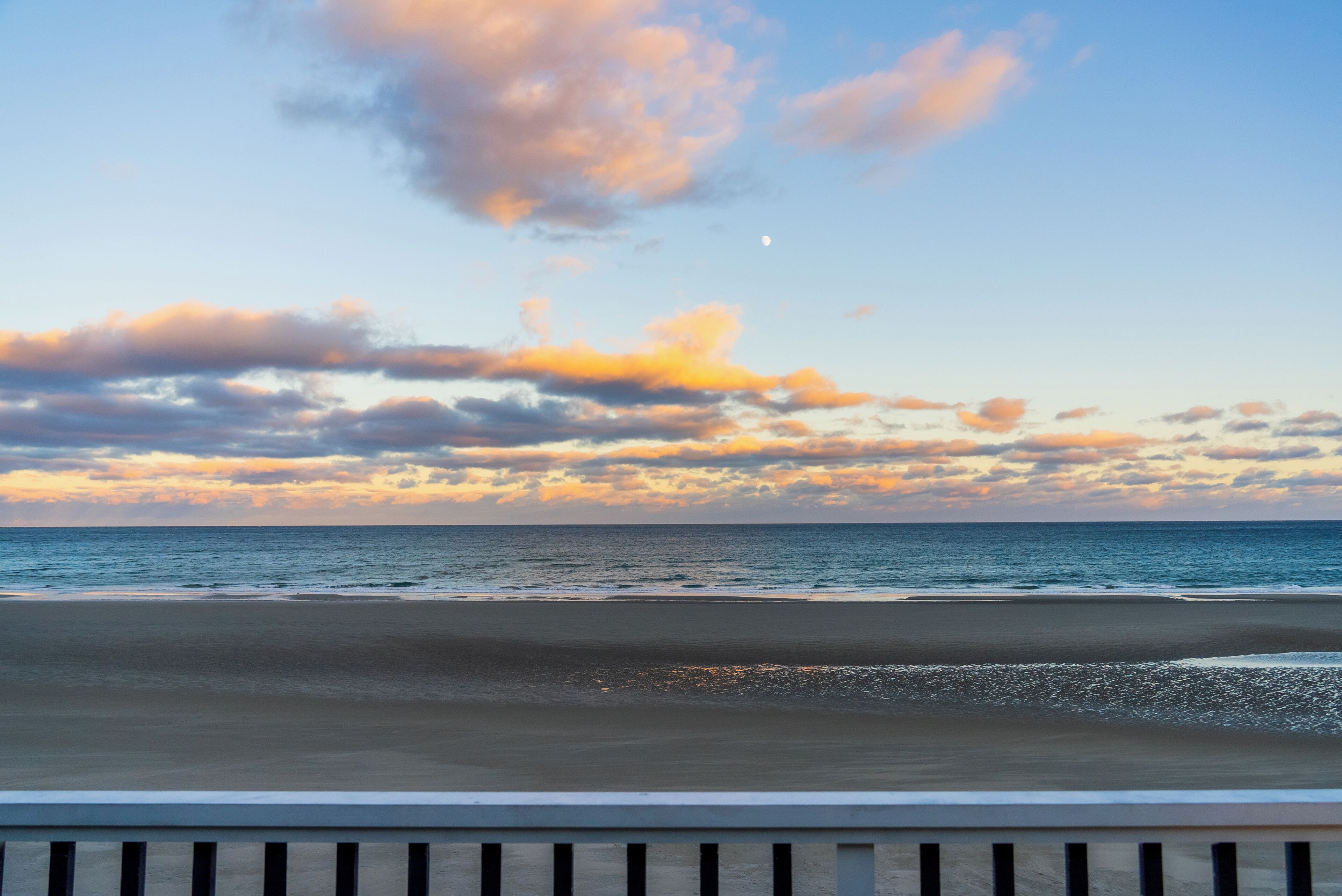 Une plage avec un ciel dégagé et une lune bien visible.