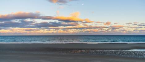 Une plage avec un ciel dégagé et une lune bien visible.