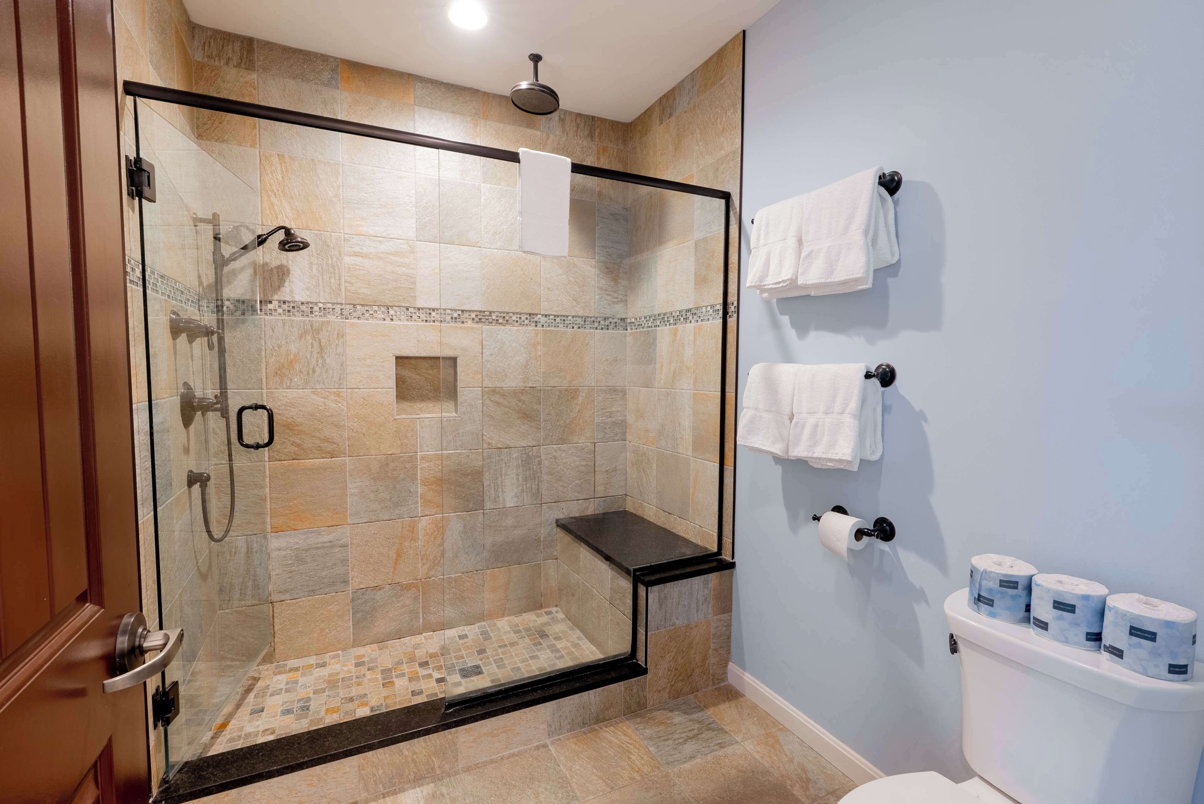 Un baño moderno con ducha envuelta en vidrio, un inodoro con toallas de papel y un perchero para toallas.