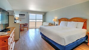 Habitación de hotel con una cama grande, televisión, escritorio con silla y vista al océano.